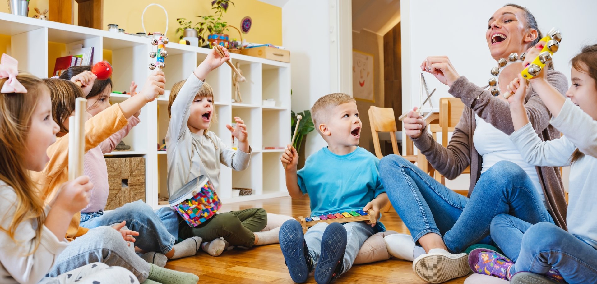 Kindergarten,Teacher,With,Children,Sitting,On,The,Floor,Having,Music
