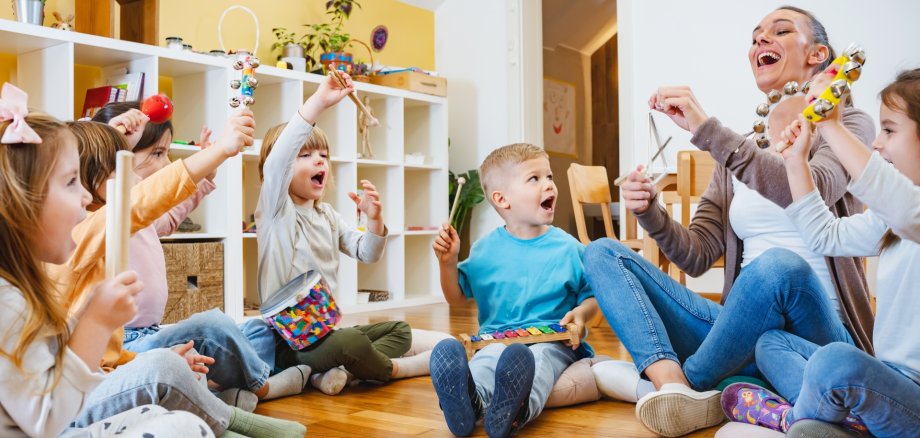 Kindergarten,Teacher,With,Children,Sitting,On,The,Floor,Having,Music