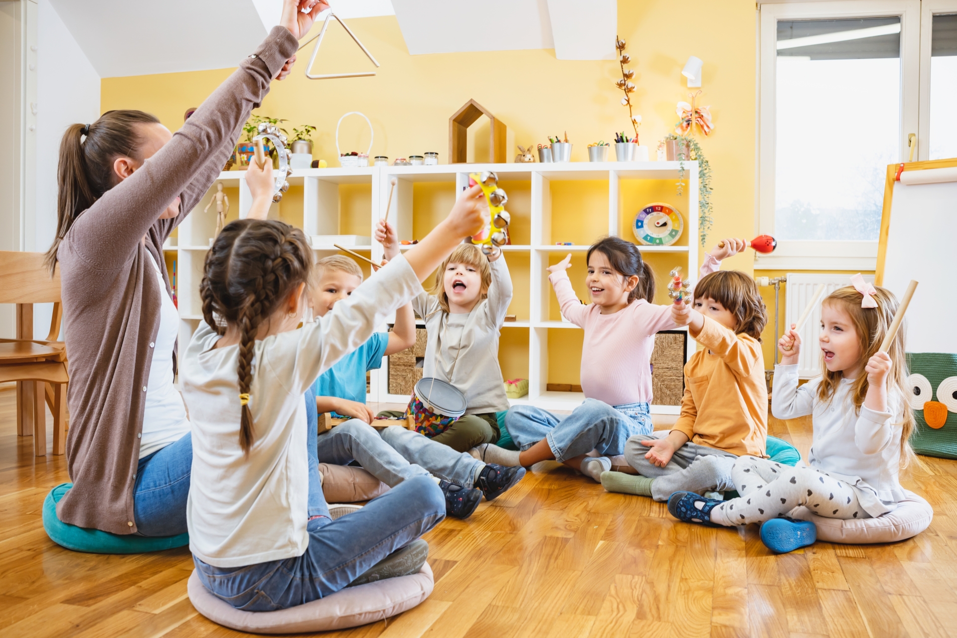Kindergarten,Teacher,With,Children,Sitting,On,The,Floor,Having,Music