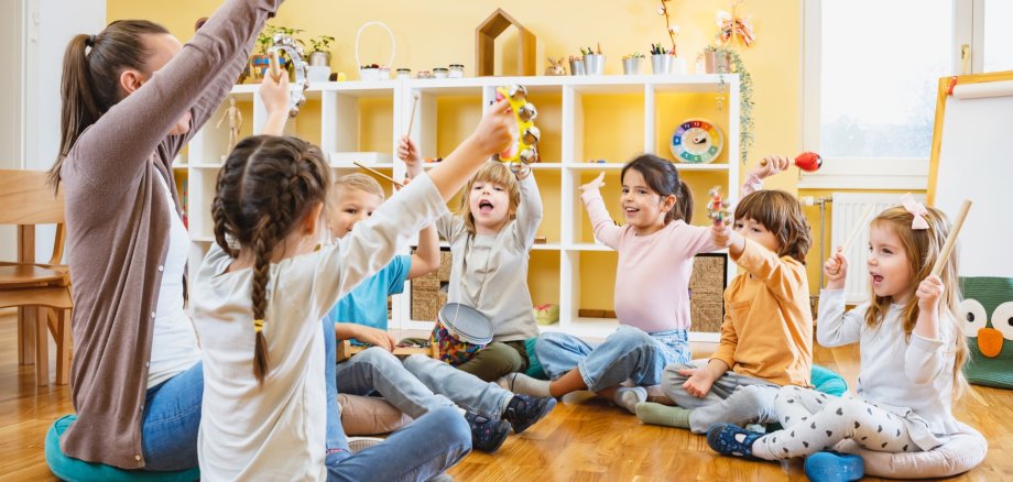 Kindergarten,Teacher,With,Children,Sitting,On,The,Floor,Having,Music